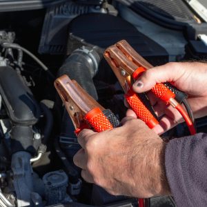 Close-up of hands holding jumper cables near a car engine, ready for repair.